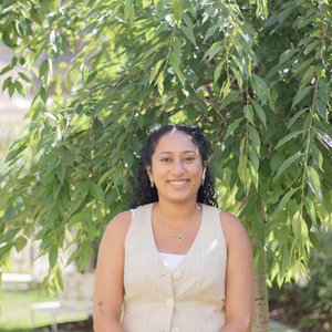 woman with long black curly hair smiling standing in front of a tree outside