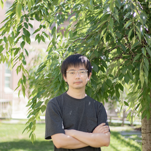 headshot of maohan su, asian man with short black hair and glasses in dark gray t shirt with arms crossed looking at camera