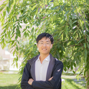 headshot of yang li, east asian man with short black hair and glasses with arms crossed smiling at camera