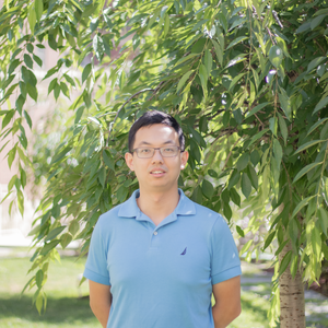 headshot of yujin bao, asian man with short black hair and glasses in blue polo shirt looking at camera