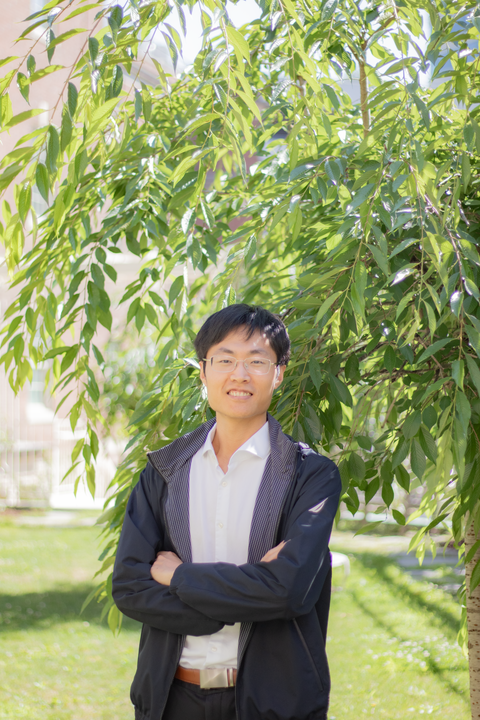 headshot of yang li, east asian man with short black hair and glasses with arms crossed smiling at camera