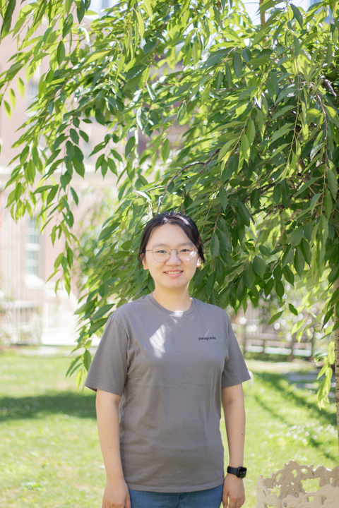 headshot of yuan tian, east asian woman with black hair pulled back and glasses in grey t shirt smiling at the camera