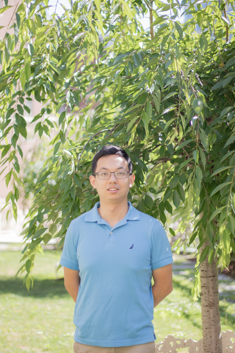 headshot of yujin bao, asian man with short black hair and glasses in blue polo shirt looking at camera