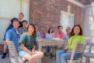 9 lab members sit around a wooden table smiling at the camera
